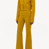 Side view of golden birch ezra bootcut jean on model wearing golden birch jacket and boots, against a white background.