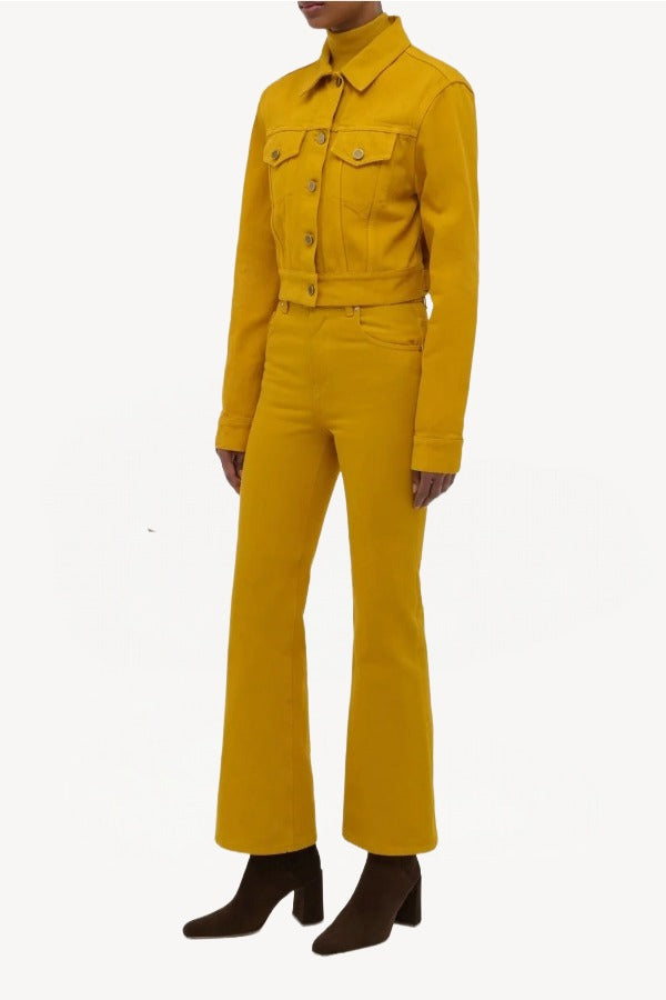 Side view of golden birch ezra bootcut jean on model wearing golden birch jacket and boots, against a white background.