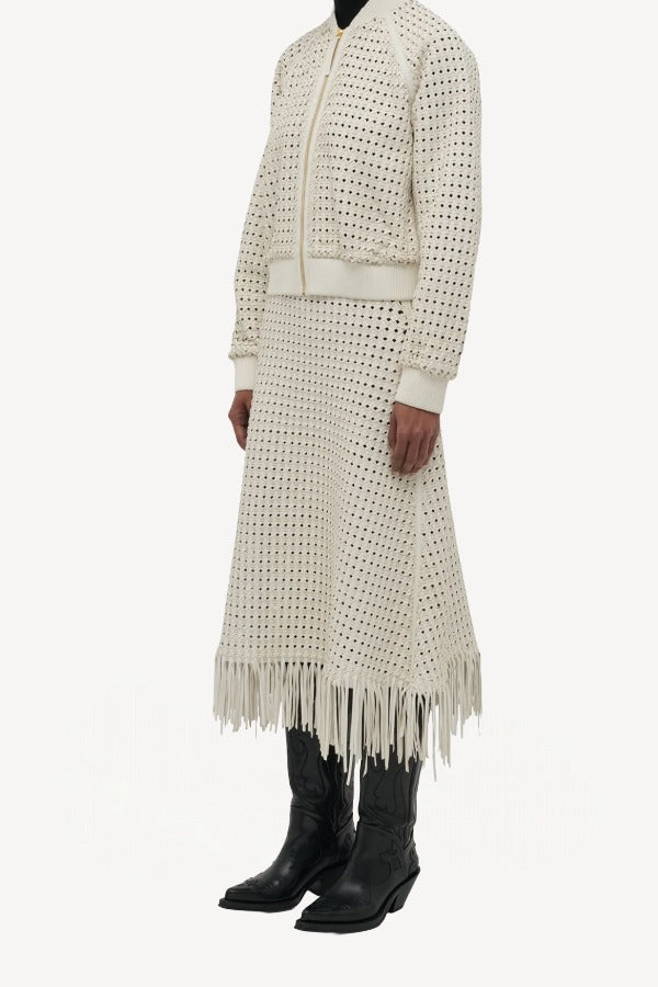 Side slanted view of white odin bomber jacket on model wearing white bennie skirt and boots, against a white background.