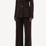 Side slanted view of chocolate vesta pant on model wearing stephanie blazer and sneakers, against a white background.