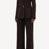 Side slanted view of chocolate vesta pant on model wearing stephanie blazer and sneakers, against a white background.