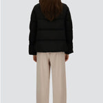 Back view of black jacket in arendelle on model wearing beige pants, against a white background.