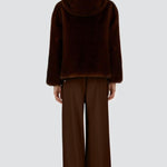 Back view of fondante knitted jacket on model wearing chocolate pants and flats, against a white background.