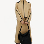 Front view of black laminar bag on model wearing yellow skirt suit and sneakers, against a white background.