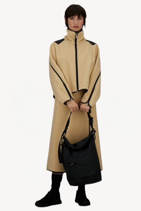 Front view of black laminar bag on model wearing yellow skirt suit and sneakers, against a white background.