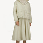 Front view of panna scuro jacket on model wearing cream skirt and sneakers, against a white background.