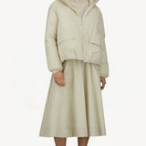 Front view of panna scuro jacket on model wearing cream skirt and sneakers, against a white background.