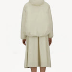 Back view of panna scuro jacket on model wearing cream skirt and sneakers, against a white background.
