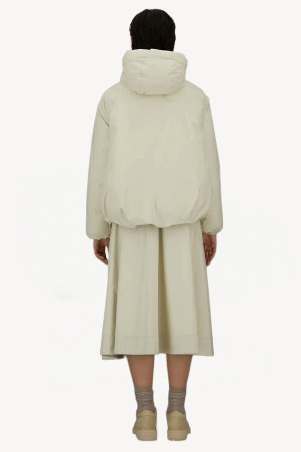 Back view of panna scuro jacket on model wearing cream skirt and sneakers, against a white background.