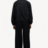 Back view of black wool jacket on model wearing black pants, against a white background.