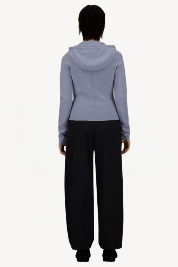 Back view of black laminar trousers on model wearing lilac top, against a white background.
