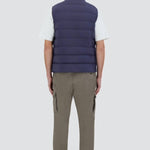 Back view of new blue gilet on model wearing green pants, white t-shirt and sneakers, against a white background.