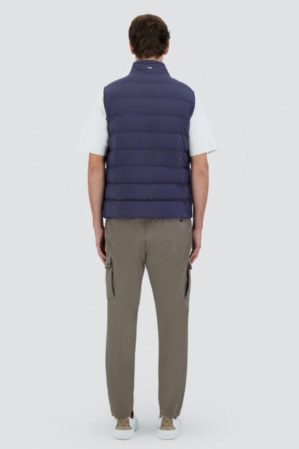 Back view of new blue gilet on model wearing green pants, white t-shirt and sneakers, against a white background.