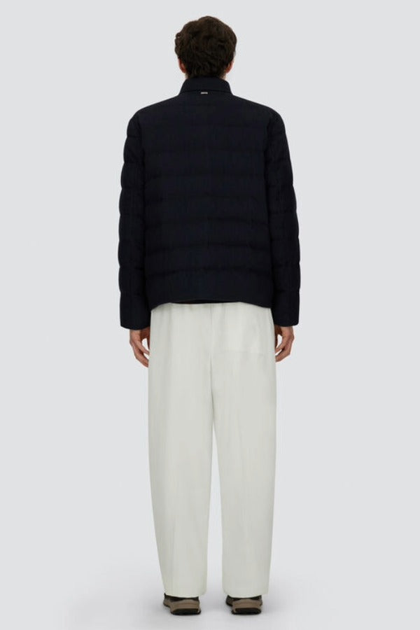 Back view of blue men's jacket on model wearing white pants and black sneakers, against a white background.