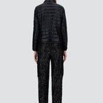 Back view of black bomber jacket on model wearing black t-shirt, trousers and mary janes against a white background.