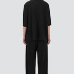 Back view of black pleated jersey t-shirt on model wearing black pants, against a white background.