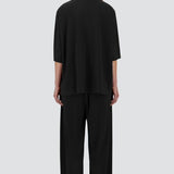 Back view of black pleated jersey t-shirt on model wearing black pants, against a white background.