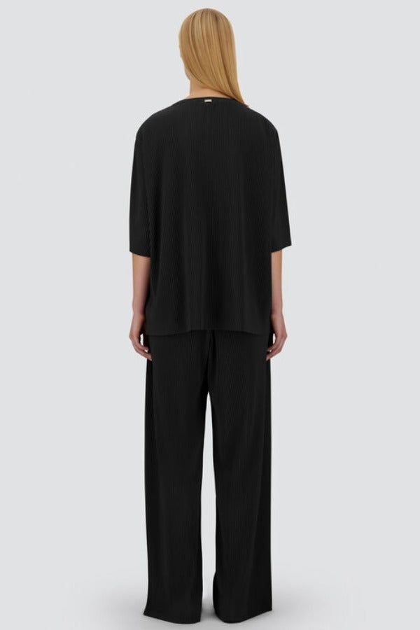 Back view of black pleated jersey t-shirt on model wearing black pants, against a white background.