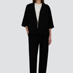 Front view of black trousers on model wearing white t-shirt and black overshirt with slippers, against a white background.