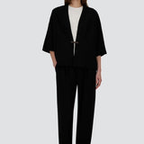 Front view of black trousers on model wearing white t-shirt and black overshirt with slippers, against a white background.