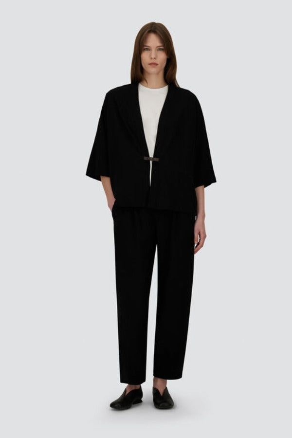Front view of black trousers on model wearing white t-shirt and black overshirt with slippers, against a white background.