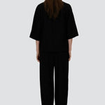 Back view of black trousers on model wearing black overshirt and slippers, against a white background.