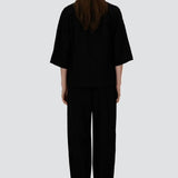 Back view of black trousers on model wearing black overshirt and slippers, against a white background.