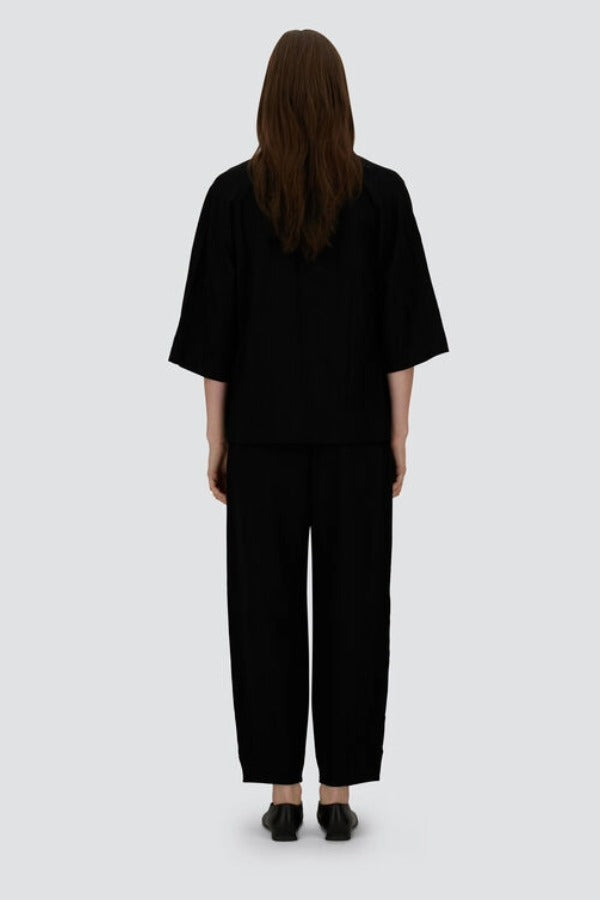 Back view of black trousers on model wearing black overshirt and slippers, against a white background.