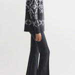 Side view of charcoal geo kick pants on model wearing grey sweater and flats, against a white background.
