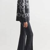 Side view of charcoal geo kick pants on model wearing grey sweater and flats, against a white background.