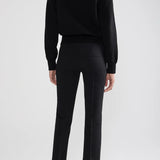 Back view of black lofty lara sweater on model wearing black pants and sandals, against a white background.