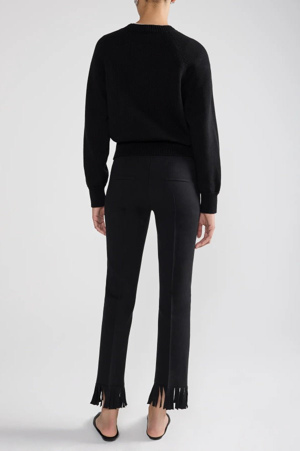 Back view of black lofty lara sweater on model wearing black pants and sandals, against a white background.