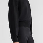 Side view of black lofty lara sweater on model wearing balck pants, against a white background.