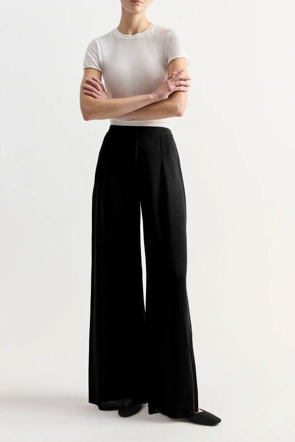 Front view of black slinky gene pant on model wearing white top and flats, against a white background.
