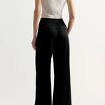 Back view of black slinky gene pant on model wearing white top and flats, against a white background.