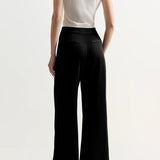 Back view of black slinky gene pant on model wearing white top and flats, against a white background.