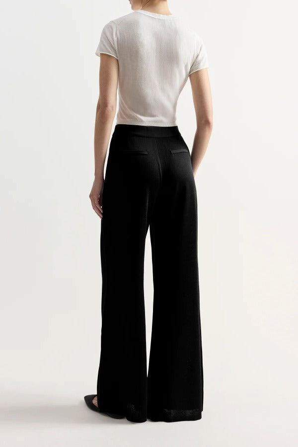 Back view of black slinky gene pant on model wearing white top and flats, against a white background.