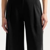 Front closeup view of black slinky gene pant on model wearing white top, against a white background.