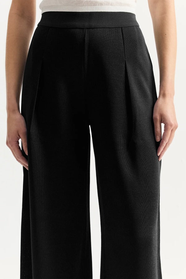 Front closeup view of black slinky gene pant on model wearing white top, against a white background.