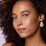 Front view of flat gold 18K YG Large Pear Drops on model, against a pink background.
