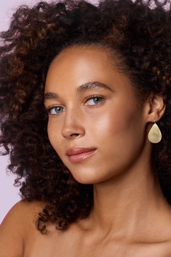 Front view of flat gold 18K YG Large Pear Drops on model, against a pink background.