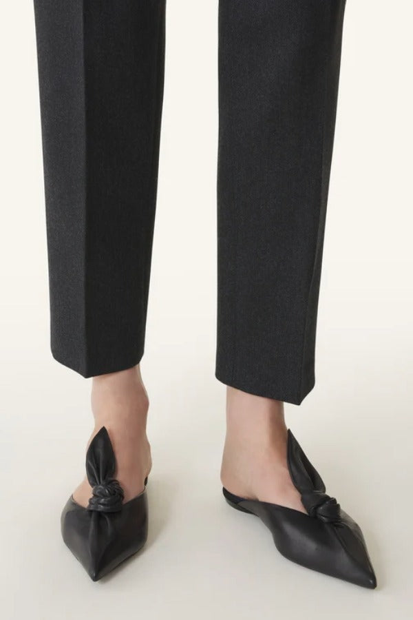 Front and side view of black flat mule bow on model wearing black pants, against a white background.