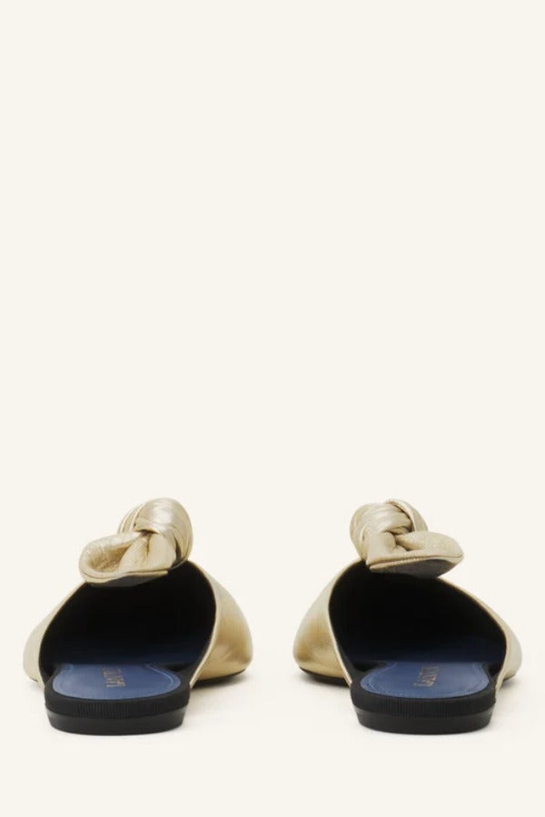 Back view of gold flat mule bow on white background, with no model shown.