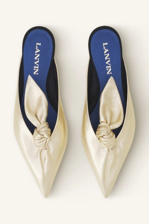 Overhead view of gold flat mule bow on white background, with no model shown.