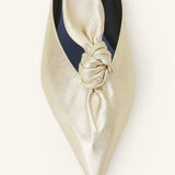 Overhead closeup of gold flat mule bow on white background, with no model shown.