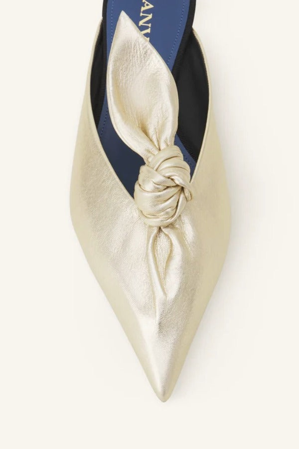 Overhead closeup of gold flat mule bow on white background, with no model shown.