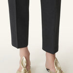 Front and side view of gold flat mule bow on model wearing black pants, against a white background.