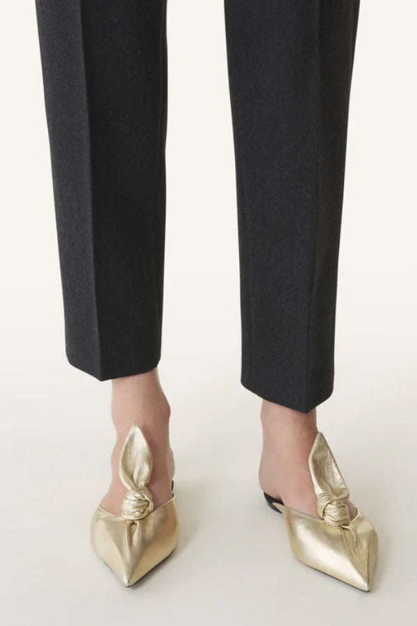 Front and side view of gold flat mule bow on model wearing black pants, against a white background.