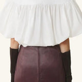 Back view of cloth puffy sleeves top on model wearing burgundy skirt, against a  white background.