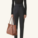 Front view of black turtleneck jumper on model wearing grey pants and flats, against a white background.